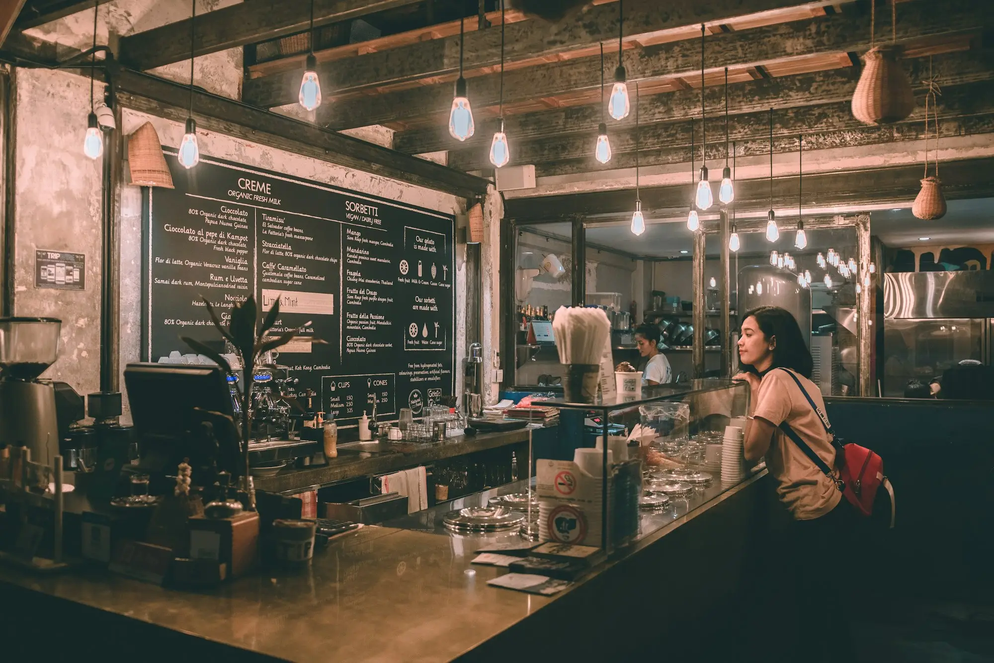 Café counter under a chalkboard price menu, where a regular customer waits to order