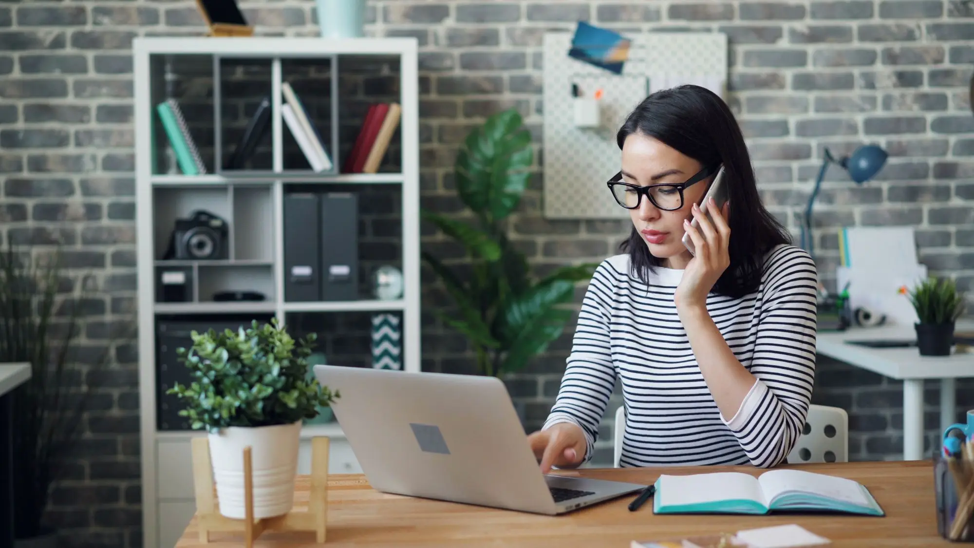 Business owner on the phone to her bank while checking the account figures on her laptop